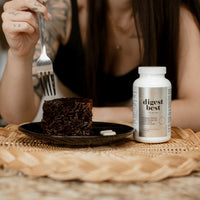 A large white bottle of Digest Best Digestive enzyme. Daily Digestive Enzyme. Decrease bloating and gas. Heartburn relief. Enhance liver health. NUsisters. 60 Capsules. Woman eating cake in the background. 60 capsules.