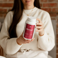 A large bottle of elever woman's multivitamin. Balance. Boost. Digestion. Energy. Renew. Refresh. 120 capsules. A woman is holding the bottle of elever.
