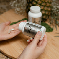 A large white bottle of Digest Best Digestive enzyme. Daily Digestive Enzyme. Decrease bloating and gas. Heartburn relief. Enhance liver health. NUsisters. 60 Capsules. A woman pouring the capsules into her hand with a second bottle in the background, a pineapple, and some flowers.. 60 capsules.