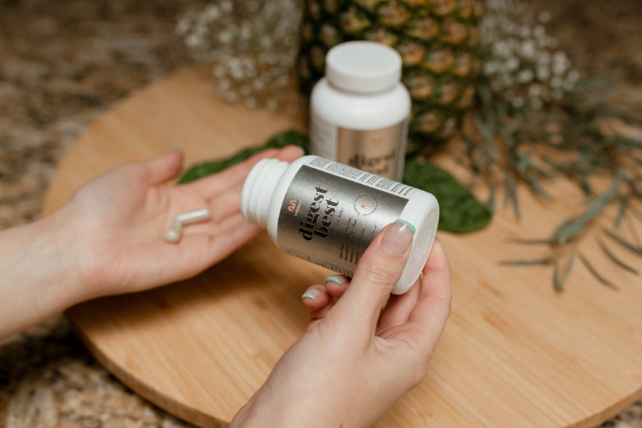 A large white bottle of Digest Best Digestive enzyme. Daily Digestive Enzyme. Decrease bloating and gas. Heartburn relief. Enhance liver health. NUsisters. 60 Capsules. A woman pouring the capsules into her hand with a second bottle in the background, a pineapple, and some flowers.. 60 capsules.