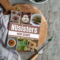 NUsisters New Start E-Cookbook on a chopping block with a  knife, spinach salad, and a tea towel.