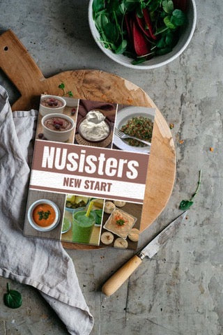 NUsisters New Start E-Cookbook on a chopping block with a  knife, spinach salad, and a tea towel.